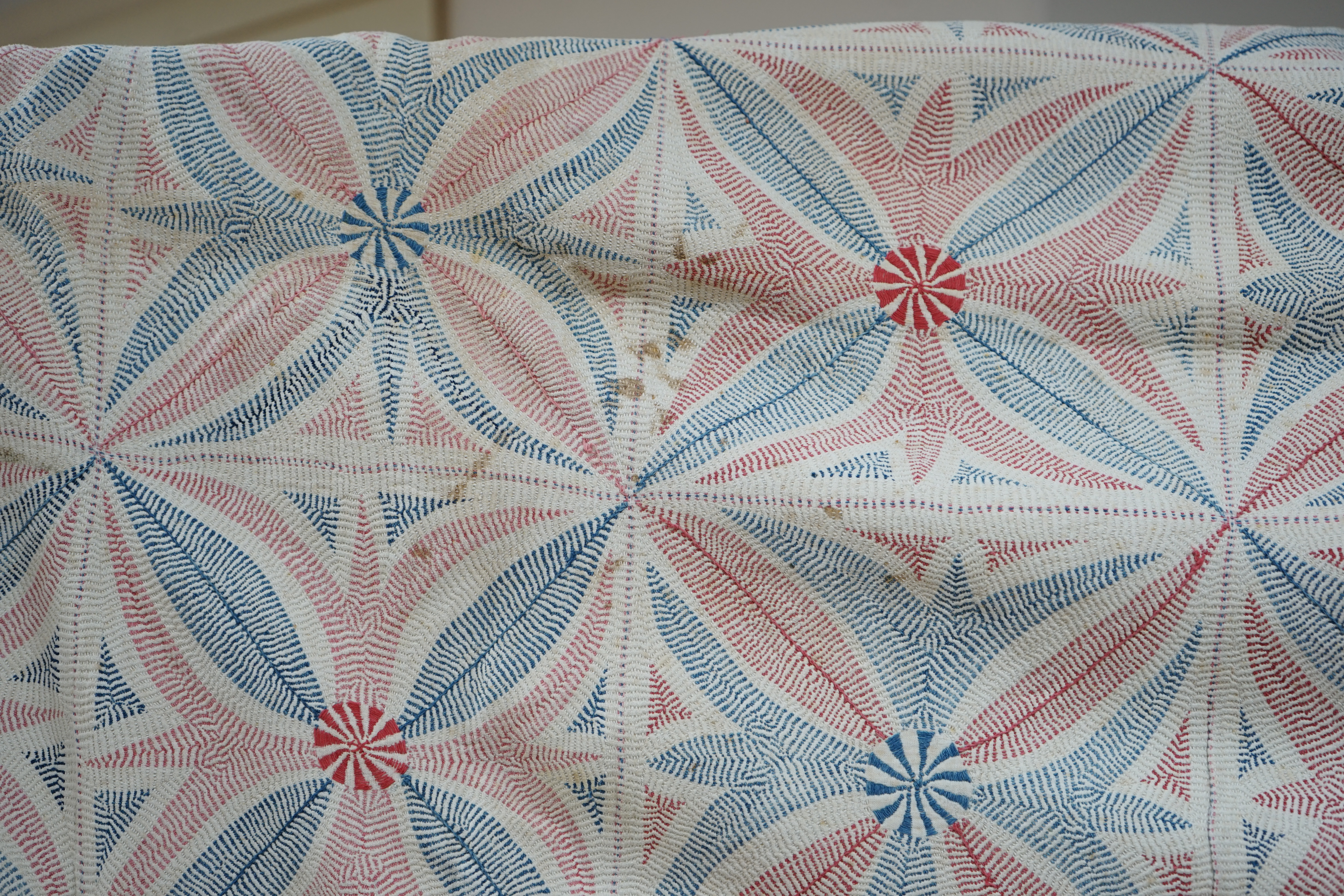 An early 20th century West Bengal Kantha embroidered quilt, embroidered on cream cloth (possibly made from layers of old saris) embroidered in blue and red threads, designed in squares of large abstracted floral motifs u